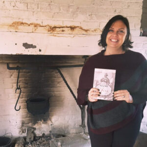 Kelley Fanto Deetz holding book in front of kitchen fireplace